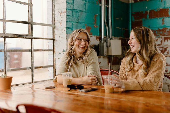 Dos amigas conversando y sonriendo mientras toman algo